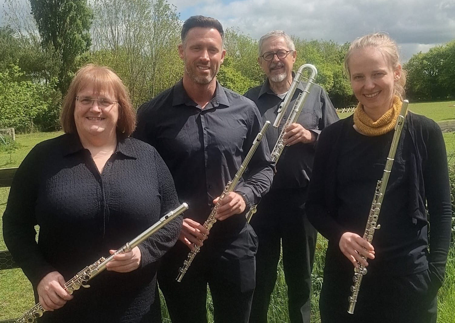 The four members of Orpheus Flutes standing outdoors holding their flutes: two concert flutes, an alto flute and a curved bass flute